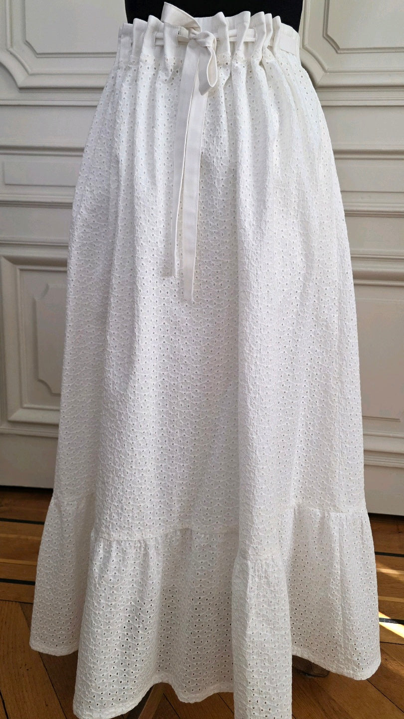 Jupe Alizé en broderie anglaise blanche, vue de face sur mannequin, avec taille haute ajustable par liens à nouer et volant en bas de jupe.