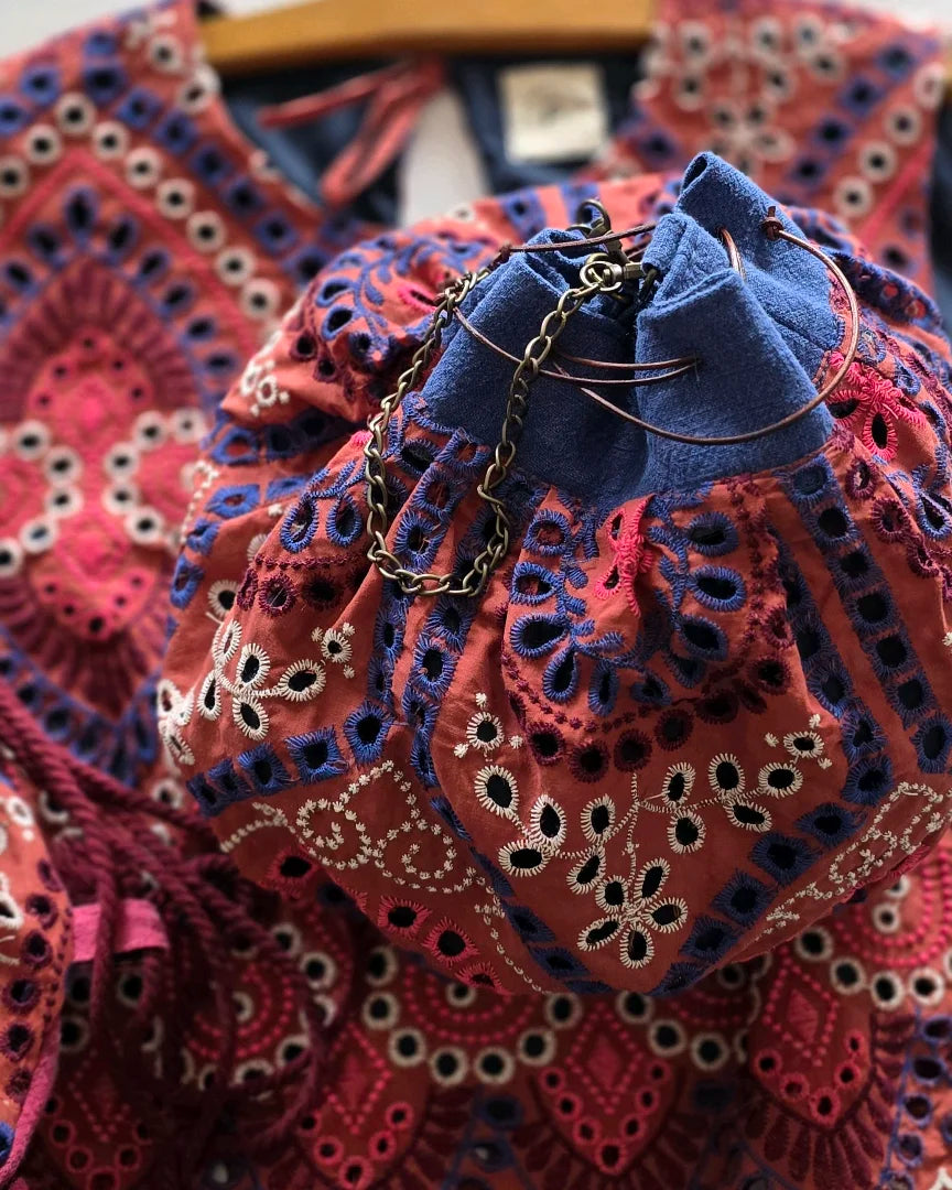 Gros plan broderie anglaise rouge et bleu sur sac bourse, texture coton ajouré et finition artisanale
