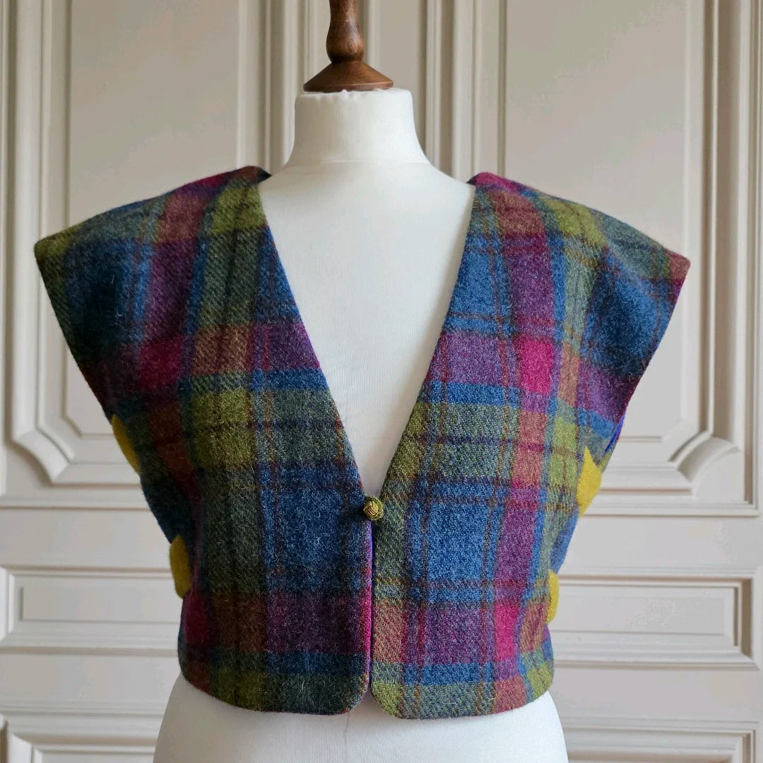 Petit boléro féminin, motifs tartans, vu de face sur mannequin devant portes banches moulurées.