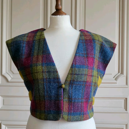 Petit boléro féminin, motifs tartans, vu de face sur mannequin devant portes banches moulurées.