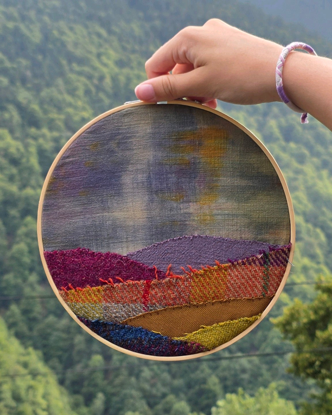 Échappée n°10, tableau textile en patchwork Harris Tweed, lin et coton de 20 cm, présenté devant un paysage. Réalisé par atelier A la du Temps Perdu 