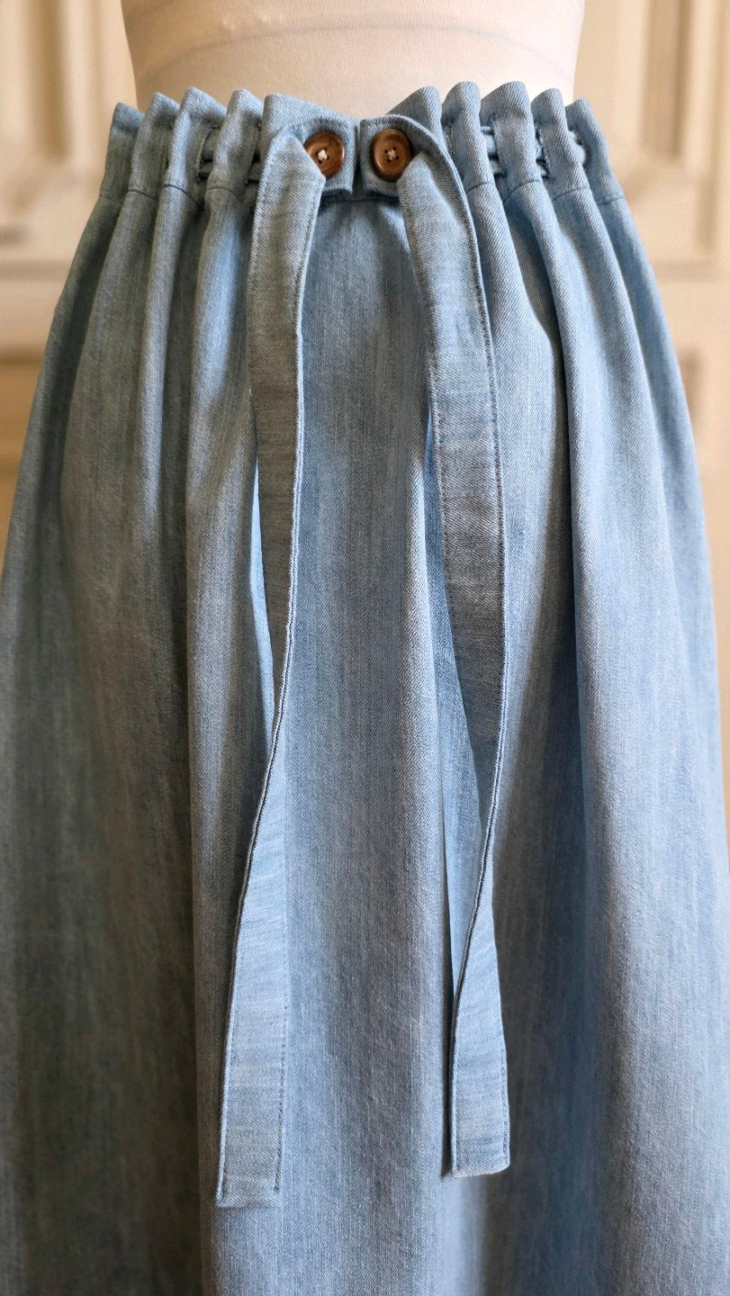 Détail de la taille ajustable de la jupe longue Bleu d'atelier avec boutons en bois, plis réglables et liens à nouer