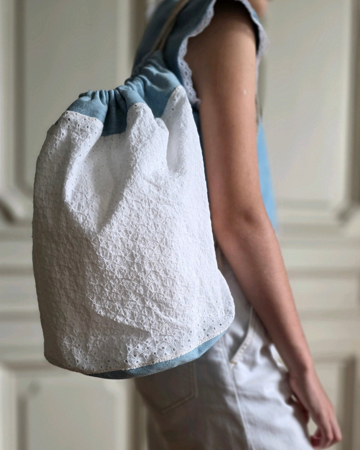 Sac baluchon en broderie anglaise blanche et denim bleu, sac seau en coton fait main porté à l'épaule.