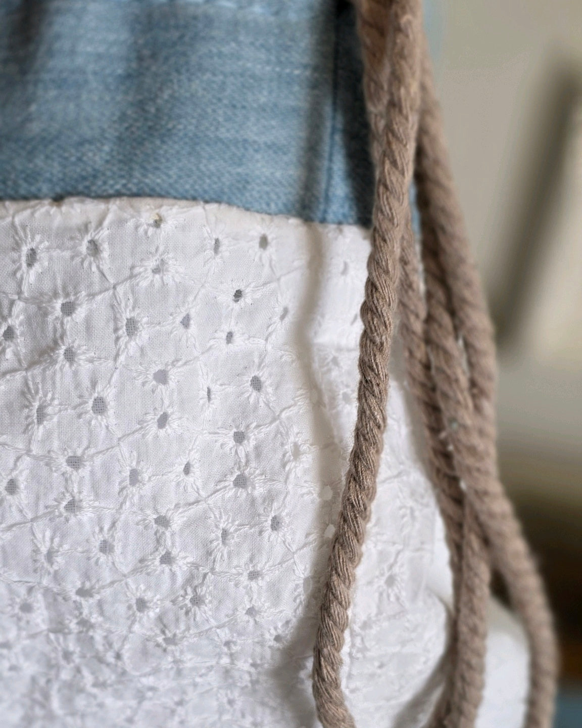 Détail de la broderie anglaise, du denim et des liens coulissants d'un sac baluchon artisanal