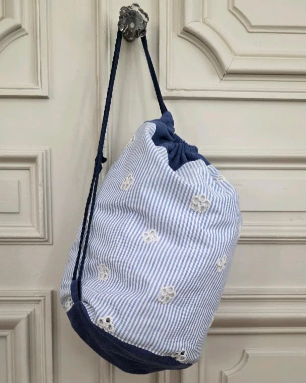 Sac baluchon broderie anglaise bleu et blanc suspendu à l’épaule, coton lin, forme souple à liens coulissants, confection artisanale