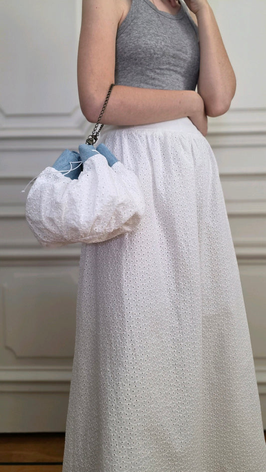 Sac bourse en broderie anglaise blanche et denim porté à l’épaule avec la jupe longue blanche en broderie anglaise assortie.