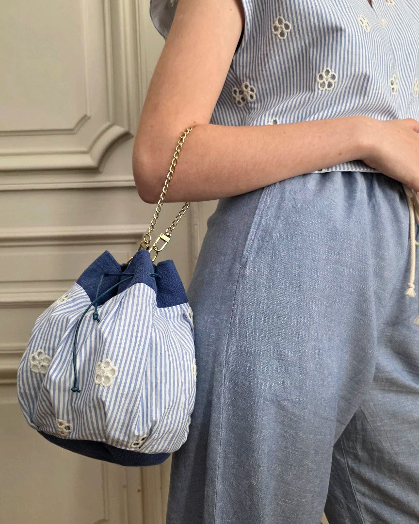 sac bourse petit modèle broderie anglaise bleu blanc porté main chaînette dorée silhouette marchant 