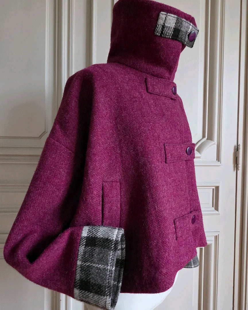 Veste femme Harris Tweed framboise 3/4 avec col montant fermé par bride tartan noir gris blanc.
Manche pliée montrant bracelet contrastant.
Photo sur mannequin devant portes haussmanniennes.