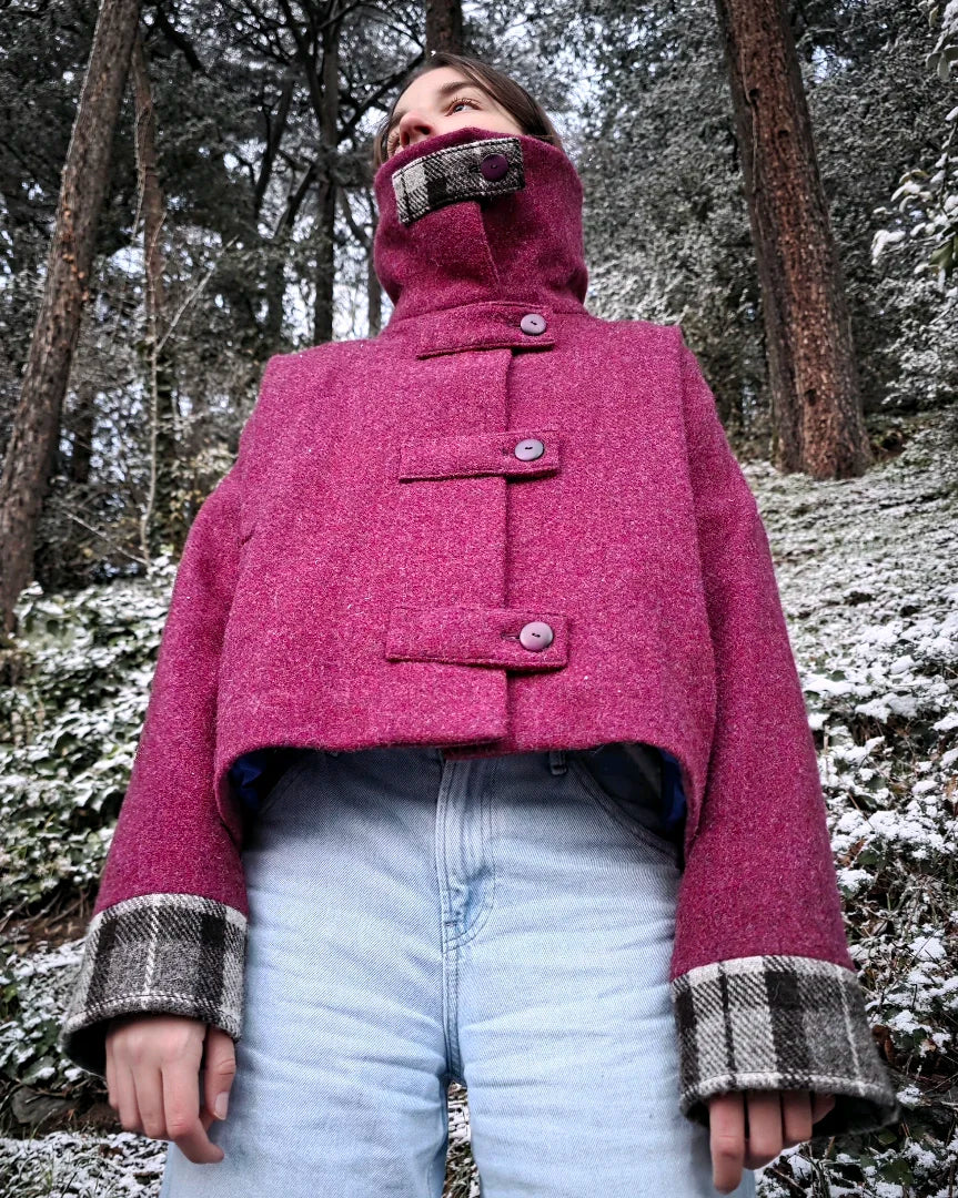 Veste Harris Tweed femme framboise portée en forêt sous la neige.
Col montant fermé, bracelets tartan visibles.
Vue de face, ambiance hivernale.
