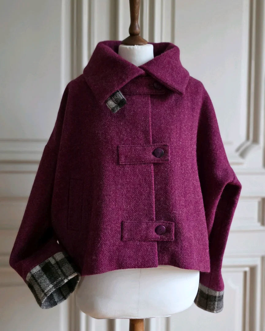 Veste Harris Tweed framboise col ouvert, bracelet de manche tartan noir gris blanc visible.
Modèle sur mannequin femme.
Fond intérieur haussmannien.