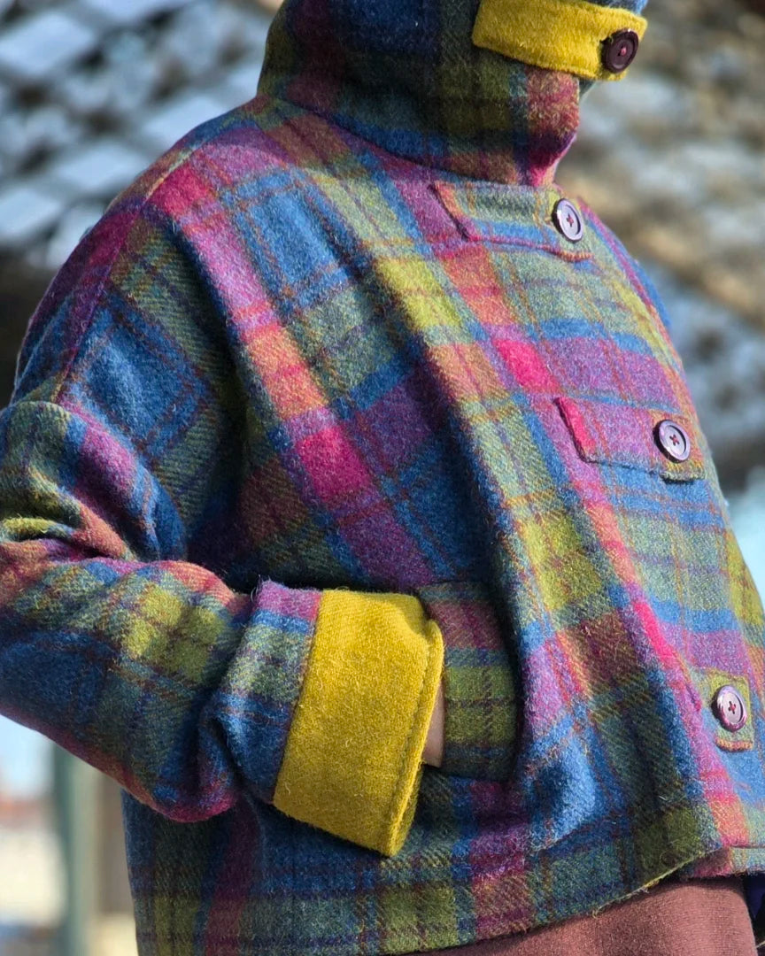 Veste Harris Tweed femme Gilberte portée en extérieur sur un quai de gare, vue 3/4, main dans la poche, bracelet de manche uni vert visible.