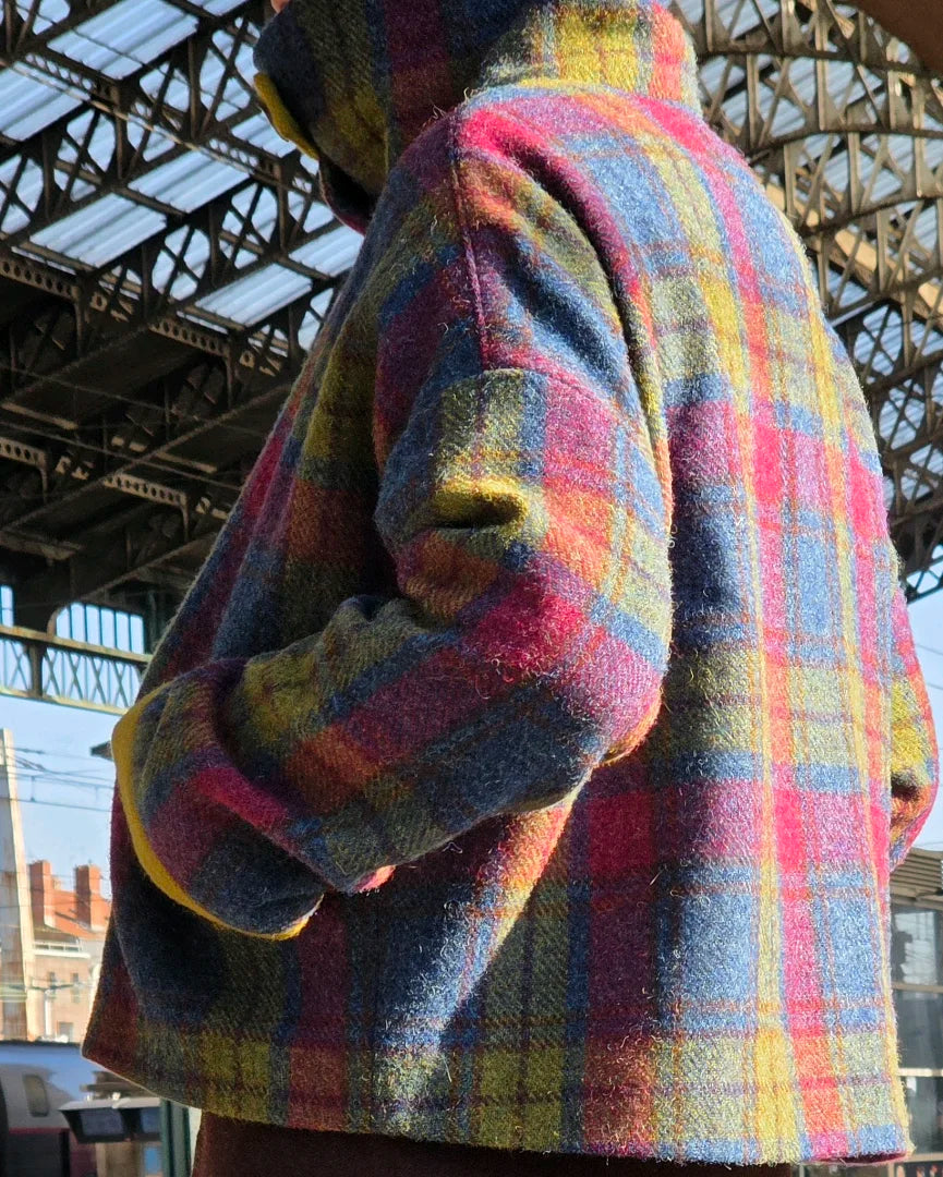 Veste Gilberte portée sur un quai de gare, vue de côté vers le dos, mettant en valeur l’épaule tombante et l’aisance de la coupe oversize.